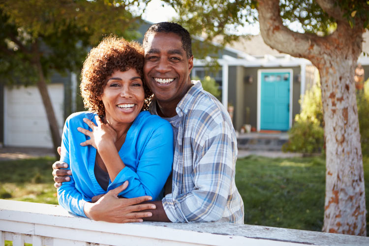 Middle-aged couple embraces and smile in front of their home after receiving professional teeth whitening