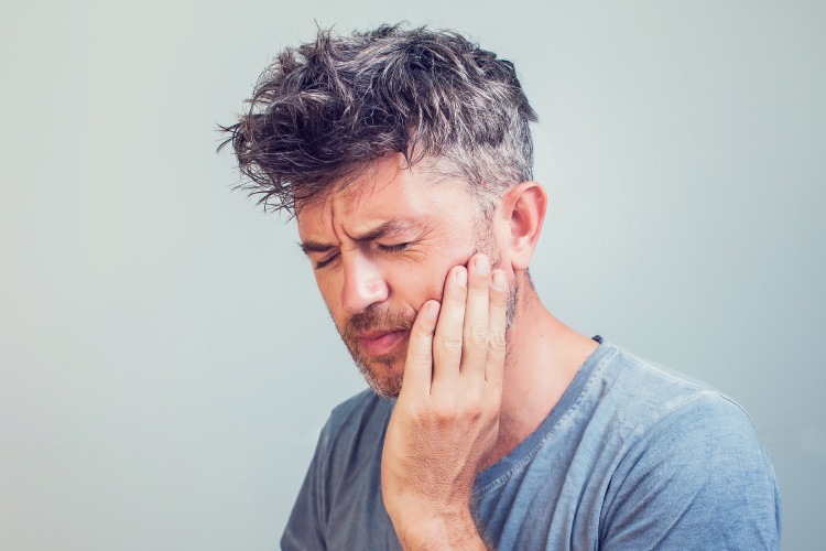 Middle-aged man cringes in pain due to a severe toothache dental emergency