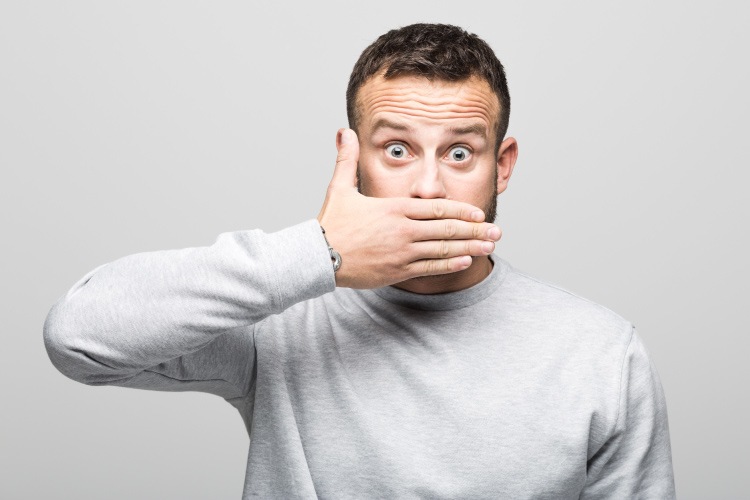 Brunette man in a gray sweater covers his mouth with his hand, saying no to dental fads