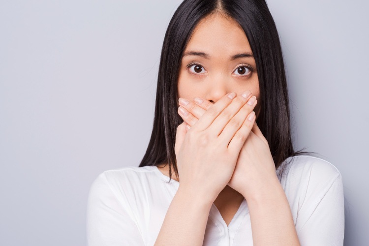 Dark-haired woman with early signs of gum disease covers her mouth with her hands