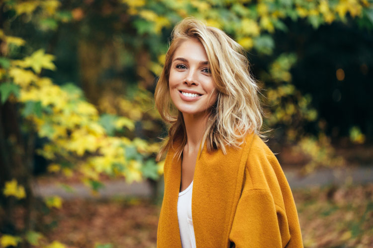 Blonde woman wears a mustard-yellow cardigan and smiles after professional teeth whitening in Westerville, OH