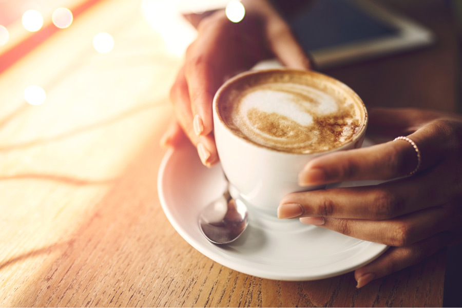 A woman's hand grip a cup of coffee on a white plate with a spoon on a wooden table