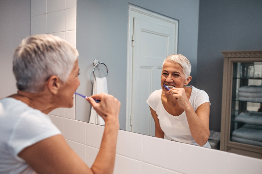 Senior woman brushes her teeth over the bathroom sink to keep her teeth and gums healthy