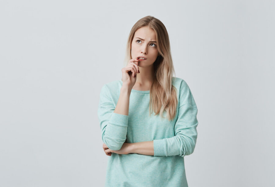 Blonde woman bites her lip and looks wonderingly because she worries that her gums are receding