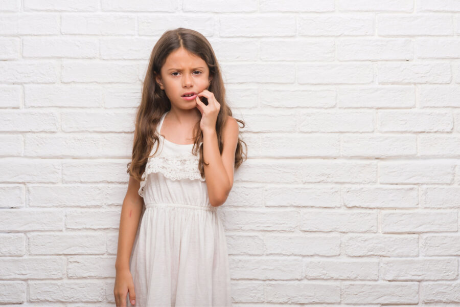 brunette little girl cringes in pain and touches her cheek due to a toothache