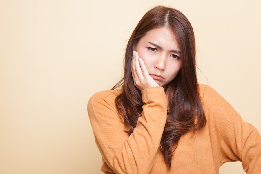 Brunette woman in a yellow sweater frowns and holds her jaw due to a toothache from sinus pressure