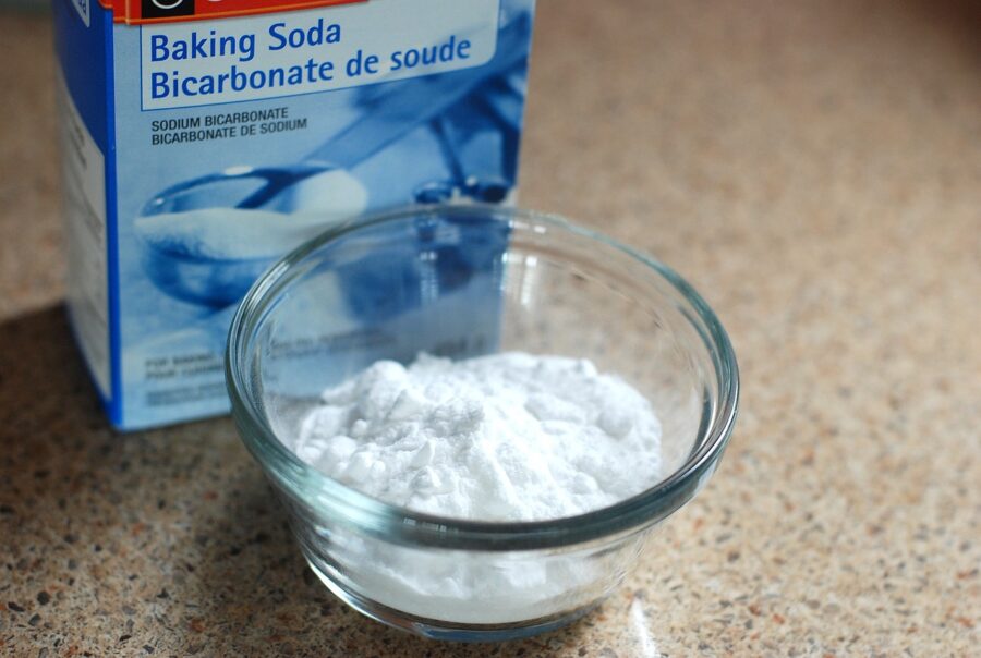 A blue box of baking soda next to a clear dish of white powder that is baking soda