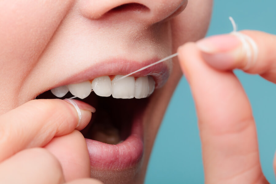 Closeup of a woman flossing her teeth with string floss against a blue background