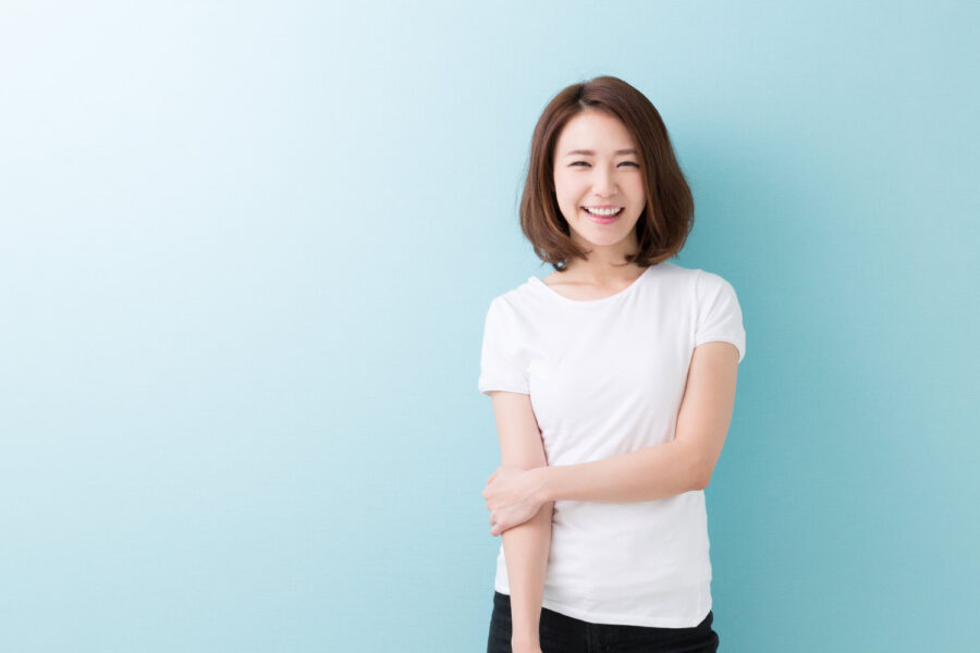 Asian woman in a white t-shirt smiles with veneers against a blue background