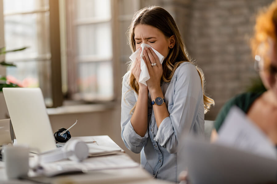 Photograph of young business woman sneezing with allergies. 