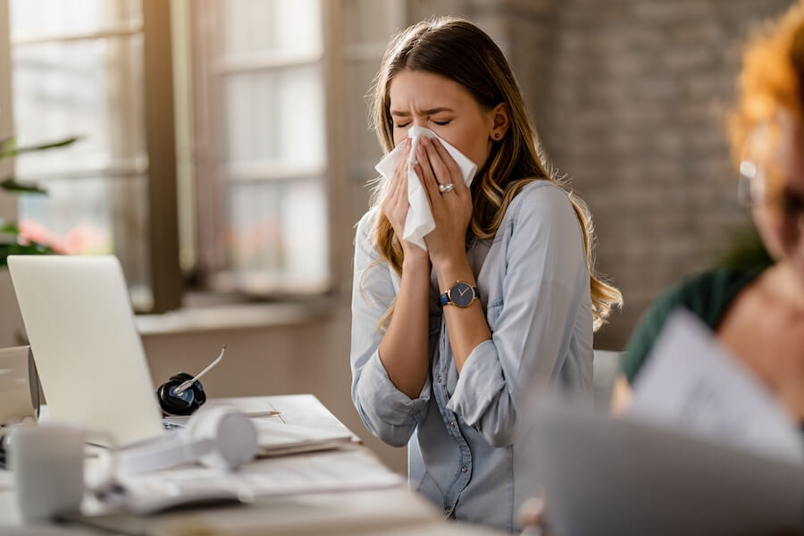 Photograph of young business woman sneezing with allergies.